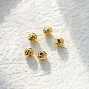 Five gold hammered metal beads with holes for DIY jewelry making on a textured background