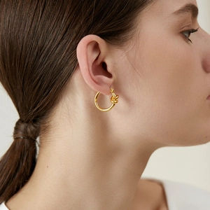 Vista detallada de modelo con aretes de aro con nudo bañados en oro de estilo minimalista