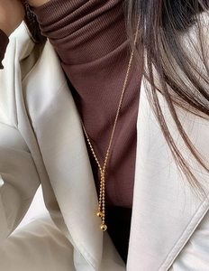 Detail einer goldenen Y-Halskette mit polierten Perlenanhängern auf Strickwaren