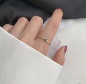 Detailansicht eines schmalen Goldrings mit rundem grünem Edelstein an einem Finger