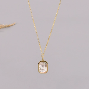Close-up of gold necklace with rectangular shell pendant and engraved time flies quote