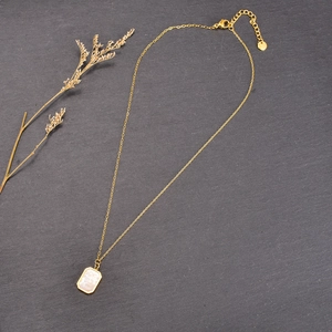 Elegant gold necklace with rectangular pendant on dark stone background with dried plant
