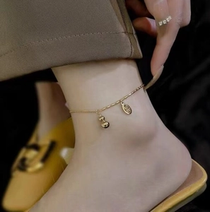 Close-up of 18K gold gourd anklet with lucky coin charm worn by model on ankle