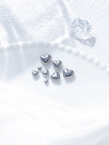 Polished stainless steel heart beads for DIY jewelry displayed on white ceramic plate