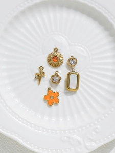 Macro shot of assorted gold DIY charms with sun, heart, and cross designs in a ceramic tray