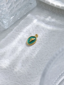 Macro shot of 18K gold plated conch pendant with teal enamel in sea-themed jewelry design