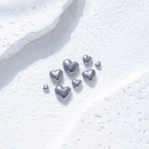 Polished silver heart charms in various sizes on white stone background for DIY jewelry