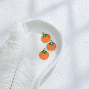 Three orange persimmon pendants with green leaves in a white ceramic tray for DIY jewelry