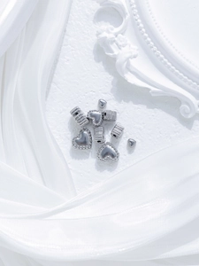 Macro view of silver heart and textured cylinder charms for DIY jewelry making