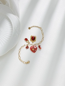 Detalle de una pulsera dorada de acero inoxidable con dijes de corazón rojo y coral