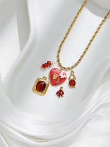 Detalle de collar de cadena dorada con colgantes de corazón y reloj rojos sobre seda blanca