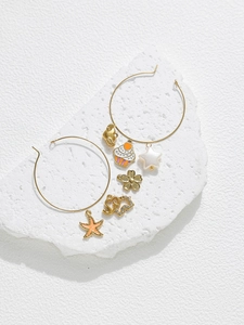 Détail de charms en émail coloré avec créoles dorées posés sur une pierre texturée