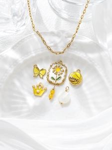 Detail of yellow enamel butterfly and sunflower charms on a gold chain over ceramic
