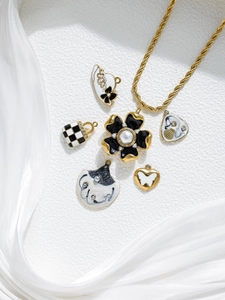 Flat lay of black and white enamel flower charms and gold rope chain jewelry pieces