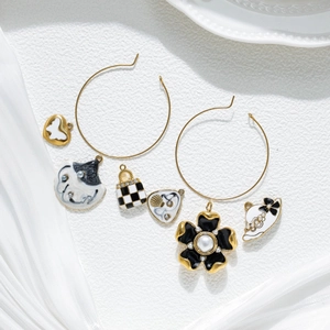 Gold hoop earrings set with flower, handbag and heart charms on white silk fabric