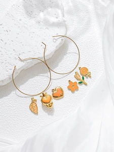 Detail view of gold hoop earrings with colorful enamel charms on white silk and stone