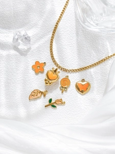 Detail of gold cross chain necklace with orange and green enamel charms on silk