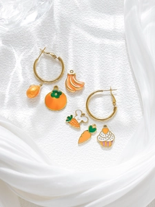 Detalle de pendientes de aro dorados con dijes de zanahoria y pastel sobre seda blanca
