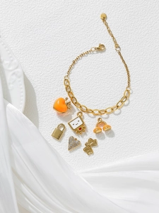Detail view of a gold charm bracelet with orange heart and cartoon pendants on white linen