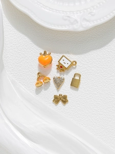 Close-up of gold-plated DIY charms including heart, bow, and robot with enamel details