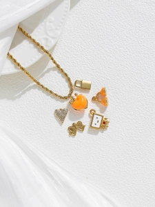 Detail of gold-plated charms including orange heart, bow, and robot on a twisted chain