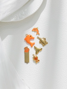 Macro view of six gold-plated ocean charms with orange enamel dolphins and sea shells