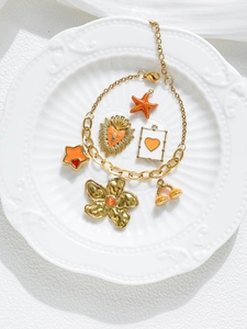 Dettaglio del bracciale a catena dorato con ciondoli a stella marina e fiori arancioni
