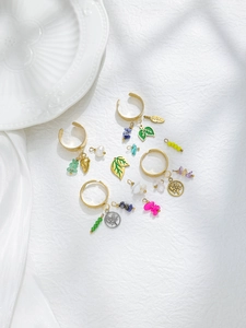 Macro shot of gold adjustable rings with enamel leaves and life tree charms on white decor