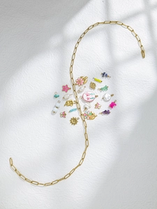 Detailopname van gouden paperclip ketting met kleurrijke bloem- en vlinderbedeltjes