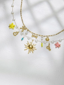 Detail of layered gold paperclip and pearl chains with starfish and sun pendants