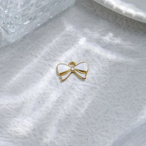 Golden bow pendant with white enamel filling for DIY jewelry making on textured background