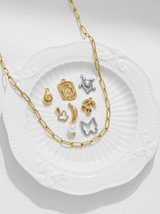 Makro-Detail einer goldenen Büroklammerkette und DIY-Schmuckanhänger auf Keramikteller