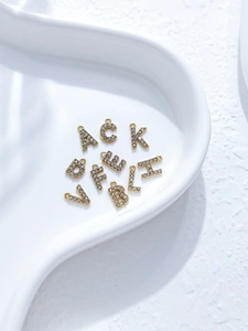 Makroaufnahme von 18K vergoldeten Buchstabenanhängern mit Kristallen auf weißem Tablett