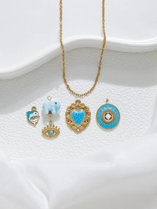 Détail de collier doré avec pendentifs cœur bleu, éléphant et œil bleu sur fond blanc