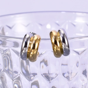 Macro detail of two-tone C-shaped hoop earrings hanging on a textured glass rim