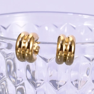 Detailed macro shot of 18K gold plated ribbed C-shape hoop earrings on a glass rim