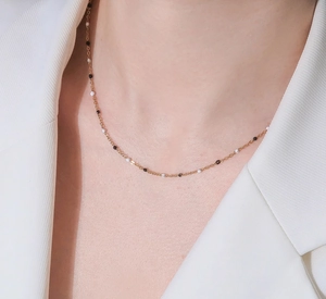 Primer plano de collar de cadena dorada con puntos de esmalte blanco y negro en modelo