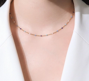 Detalle de collar dorado con cuentas azules y blancas en una modelo con chaqueta blanca