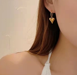 Minimalist gold heart dangle earrings on model featuring a 3D polished stainless steel design