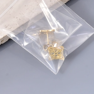Detailansicht der 18K vergoldeten Hexenknoten Ohrstecker in einer Klarsichtverpackung