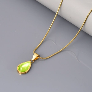 Detail van groene waterdruppel hanger met gouden slangenketting op grijze achtergrond