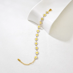 Detailopname van witte en gele madeliefje emaille bedeltjes op gouden armband