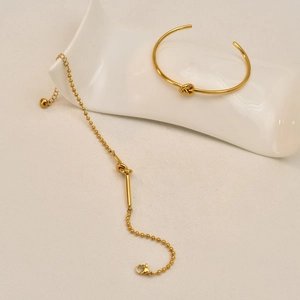 Gold-plated knot jewelry set featuring a cuff bangle and bead chain bracelet on a white tray