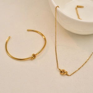 Gold knot jewelry set with necklace and open cuff bracelet on elegant white decor