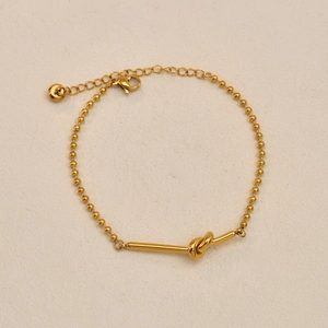 Detail of gold-plated beaded bracelet featuring a knotted tube charm and lobster clasp