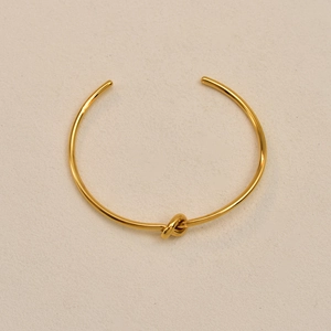 Detailed macro view of minimalist gold knot cuff bangle with polished mirror finish surface