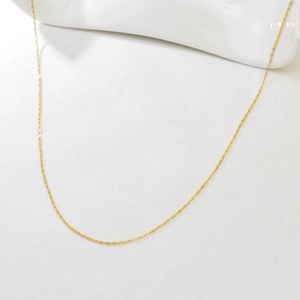Macro detail of adjustable gold cable chain necklace on a clean white ceramic background