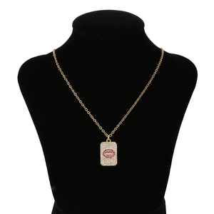 Détail du pendentif doré rectangulaire avec cristaux et lèvres roses sur buste noir