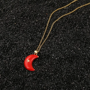 Detalle de un colgante de luna de esmalte rojo con estrella dorada sobre fondo negro
