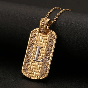 Detalle del colgante chapa dorada con letra L, textura tejida y microcirconitas